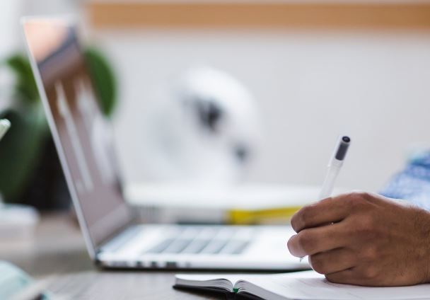 Person sitting at a laptop with a pen in their hands