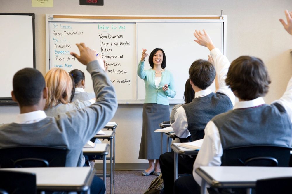 Teacher in a classroom calling on students with raised hands